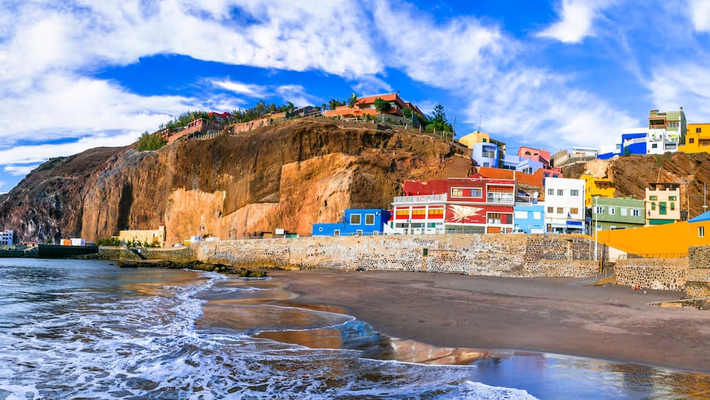 A coastal town with colorful buildings, a rocky cliff, and a beach.