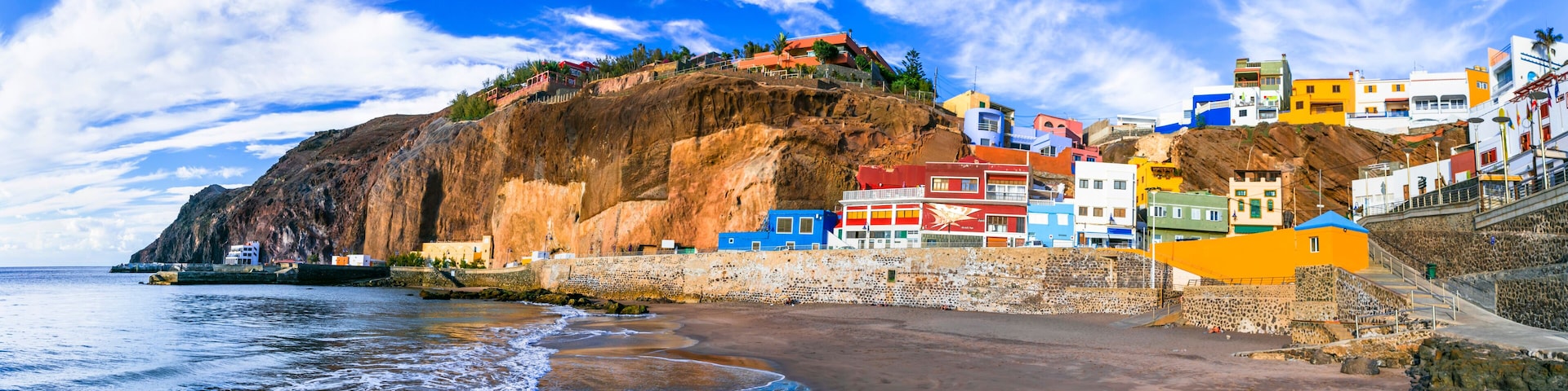 Un pueblo costero con edificios de colores, un acantilado rocoso y una playa.