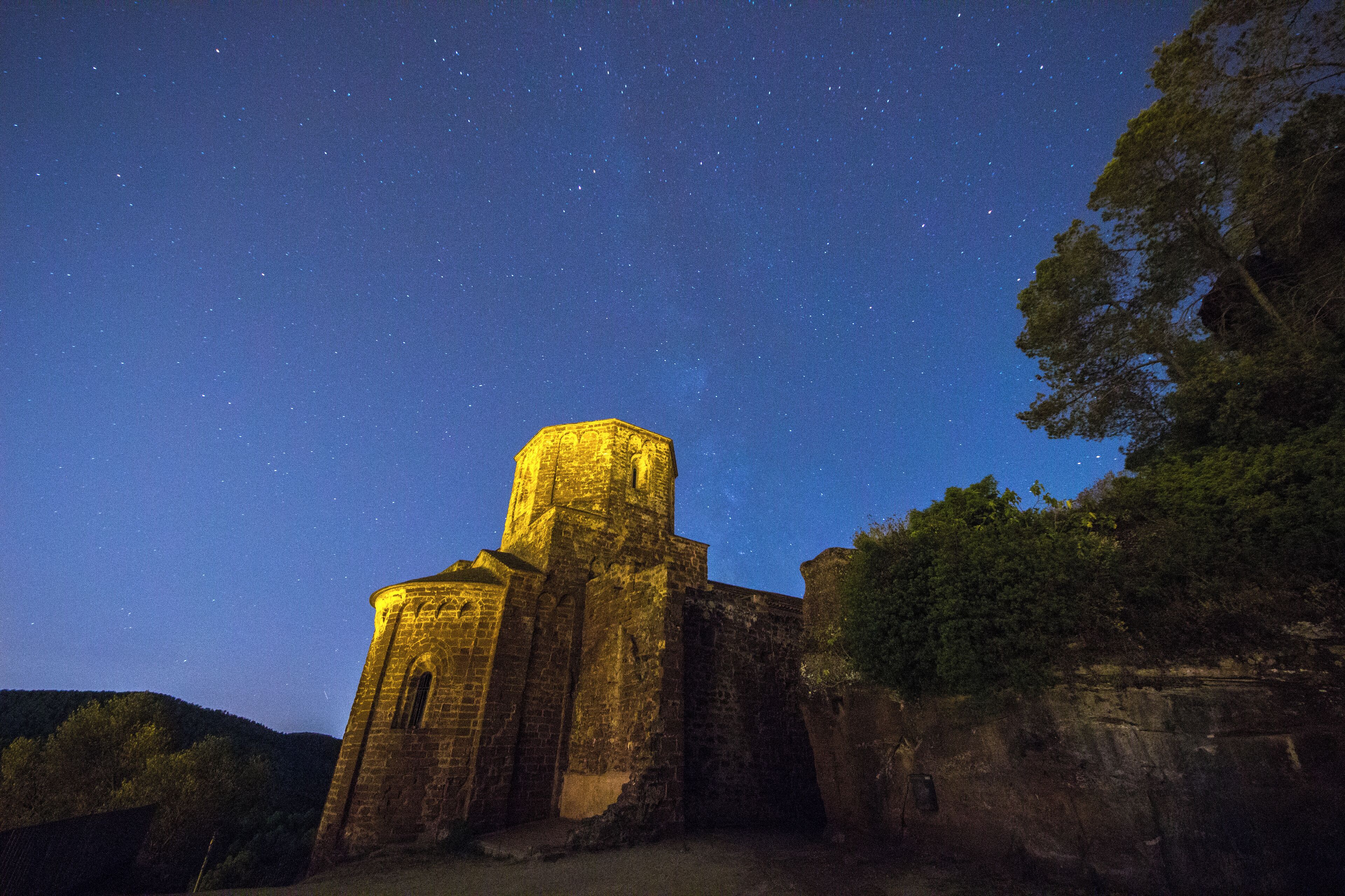 A historic stone church with a bell tower under a starry night sky.
