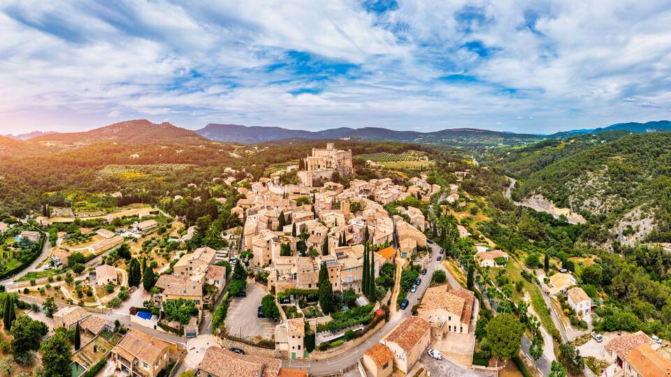 A panoramic view of a historic town with a prominent castle-like structure surrounded by lush greenery and rolling hills.