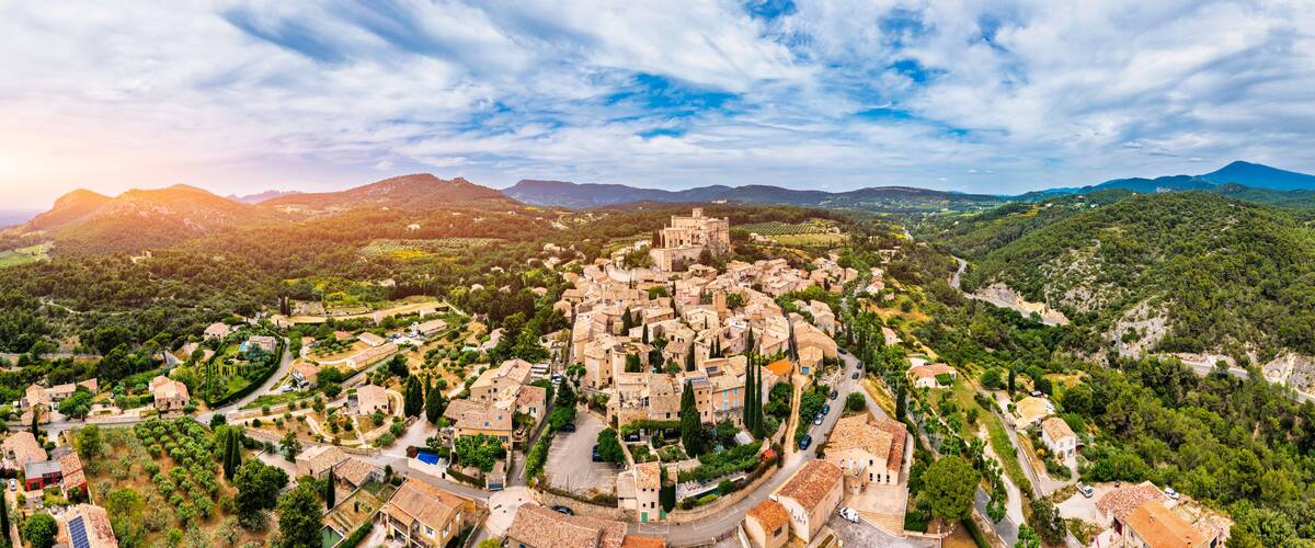 A panoramic view of a historic town with a prominent castle-like structure surrounded by lush greenery and rolling hills.