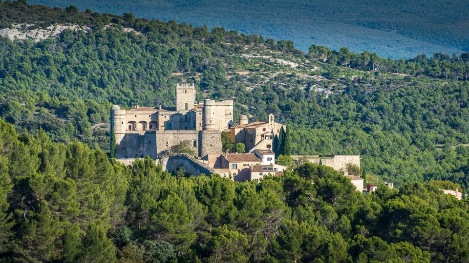 A historic castle surrounded by dense forest and hills.