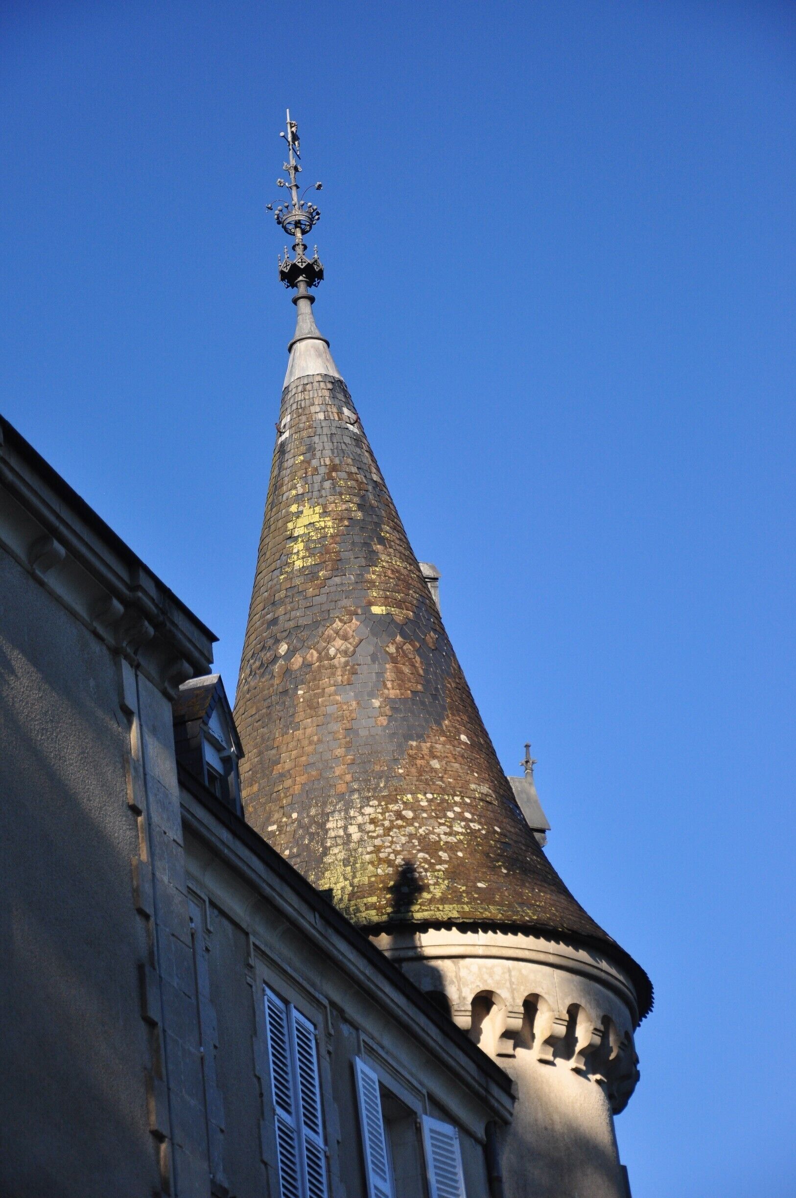 A tall, conical tower with a weather vane on top, set against a clear blue sky.