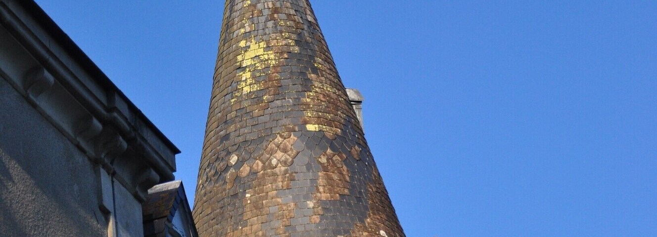 A tall, conical tower with a weather vane on top, set against a clear blue sky.