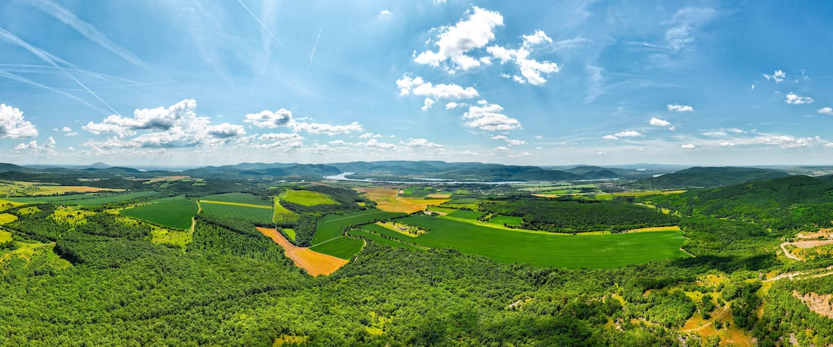 A panoramic view of a lush green valley with rolling hills, a river, and a distant body of water.