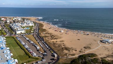 Un pueblo costero con playa, coches aparcados y edificios a lo largo de la costa.