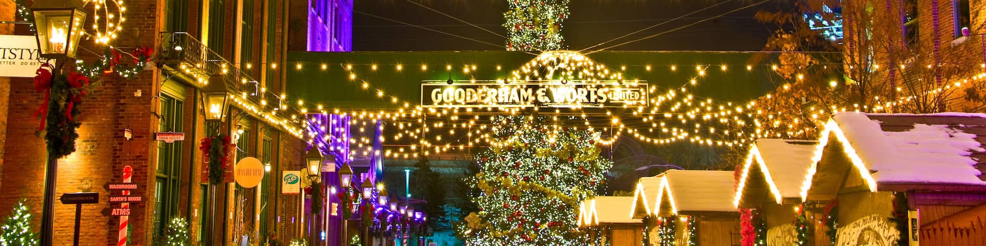 A festive street with string lights, a large Christmas tree, and holiday decorations.