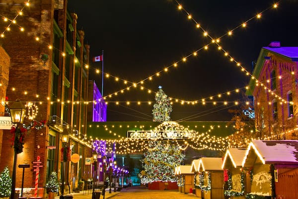Une rue animée, illuminée de guirlandes lumineuses, avec un grand sapin de Noël et des décorations de fêtes.