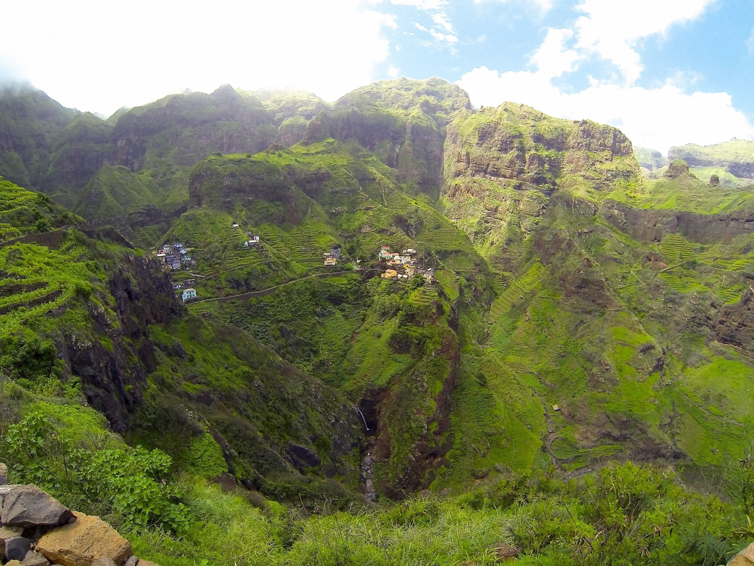 A lush green valley with terraced fields and scattered houses.