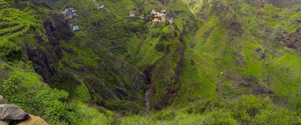 A lush green valley with terraced fields and scattered houses.