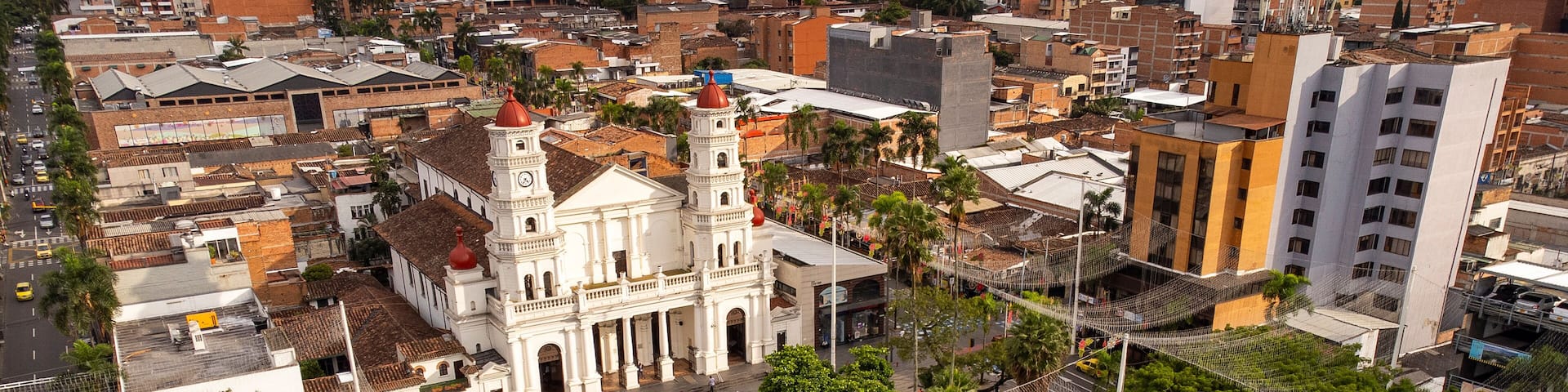 A cityscape with a prominent white church with a clock tower, surrounded by lush greenery and a pedestrian bridge.