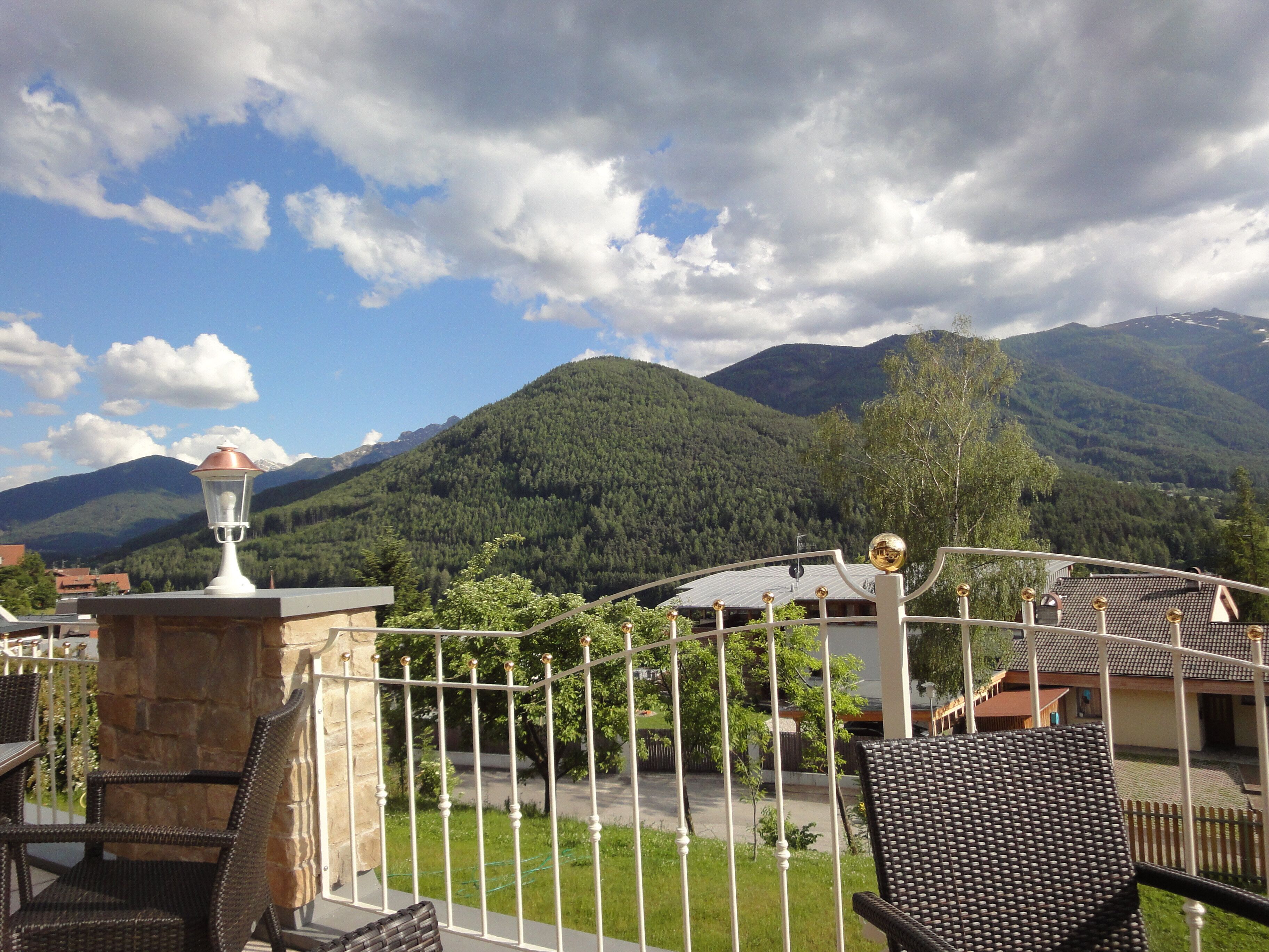 A balcony with wicker chairs, a metal fence, and a mountain landscape in the background.