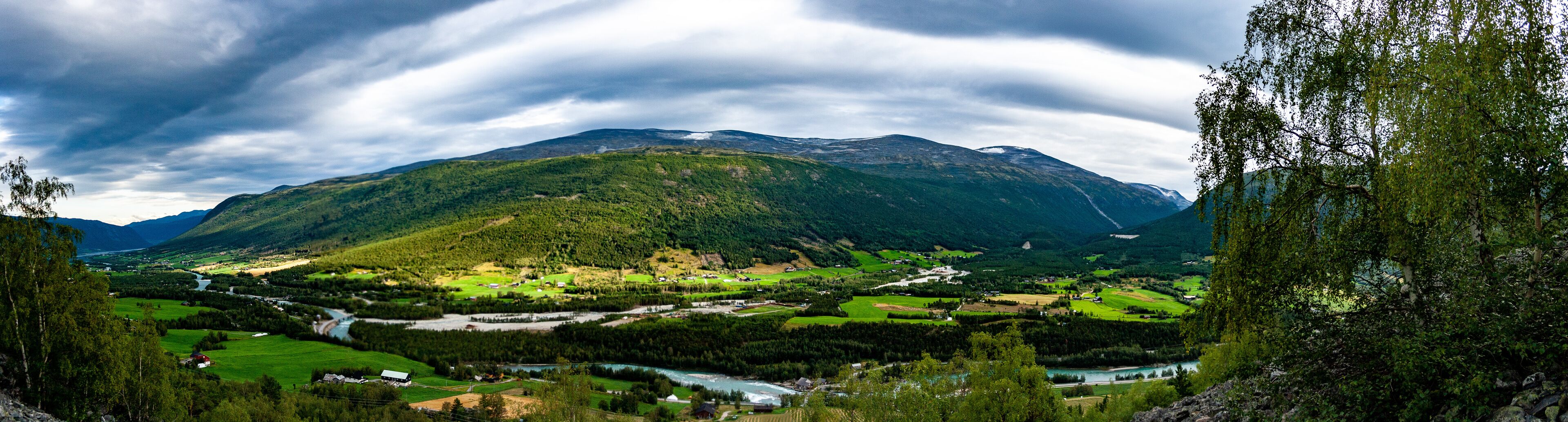 A mountainous landscape with a river flowing through a valley, surrounded by green fields and scattered houses.
