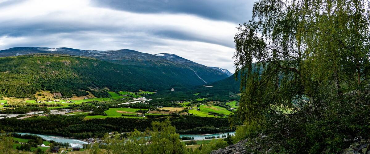 A mountainous landscape with a river flowing through a valley, surrounded by green fields and scattered houses.