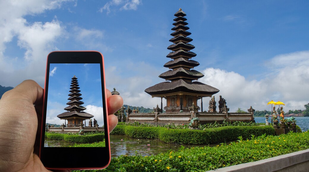 View over the mobile phone display. Holding the mobile phone in hands and taking a photo. Pura Ulun Danu Batur is hindu temple at Bratan lake in Bali, Indonesia.