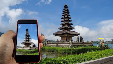 View over the mobile phone display. Holding the mobile phone in hands and taking a photo. Pura Ulun Danu Batur is hindu temple at Bratan lake in Bali, Indonesia.