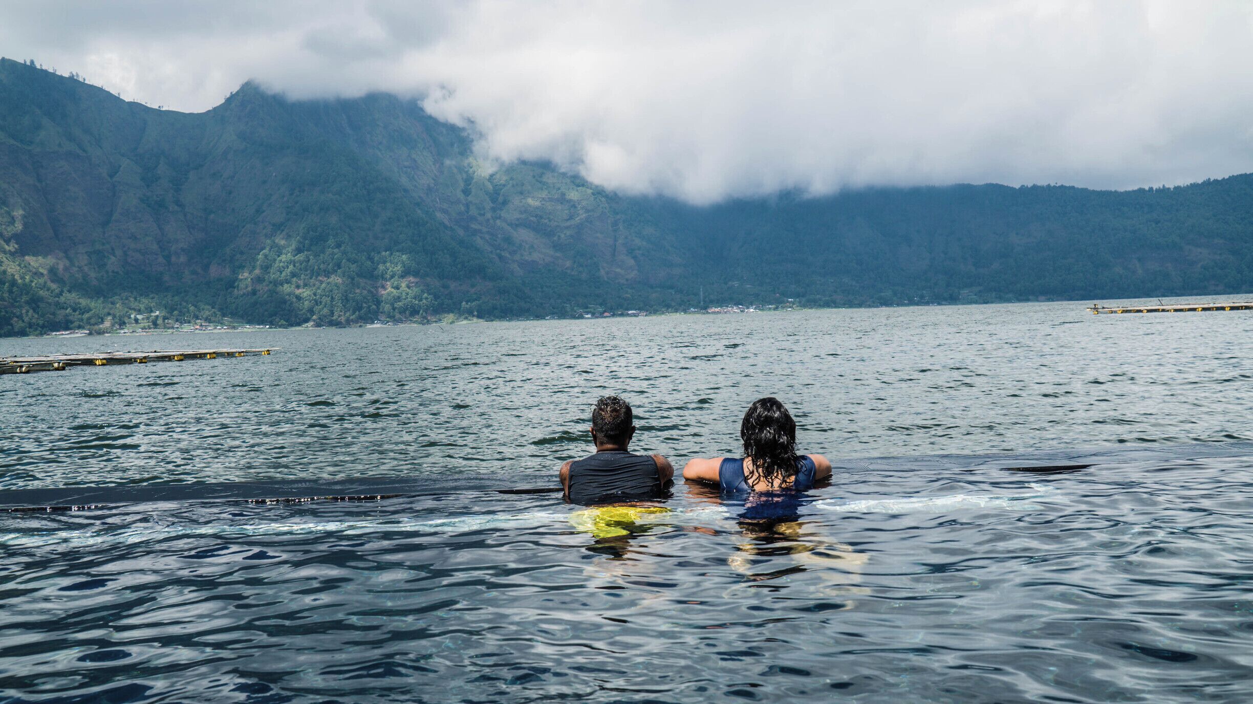 Two people in a lake with mountains in the background.