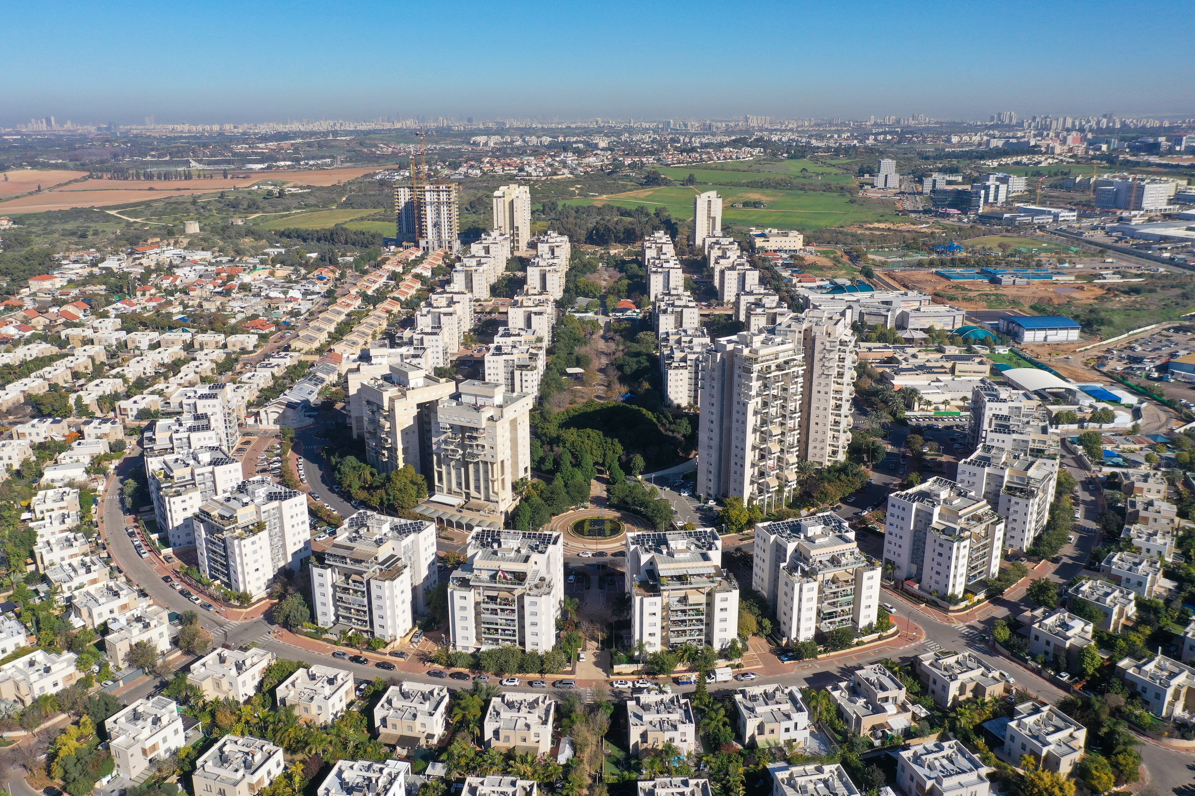 An aerial view of a densely populated urban area with high-rise residential buildings, a central roundabout, and surrounding green spaces.