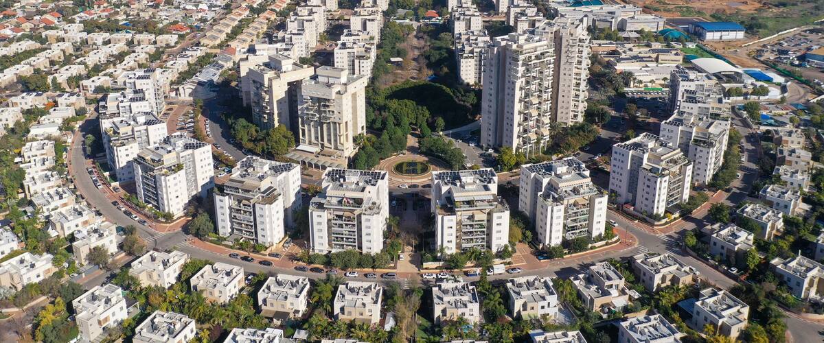 An aerial view of a densely populated urban area with high-rise residential buildings, a central roundabout, and surrounding green spaces.