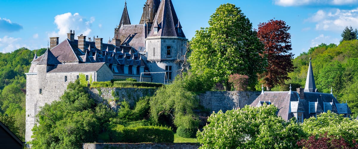 A historic castle with multiple towers, surrounded by lush greenery and a clear blue sky.