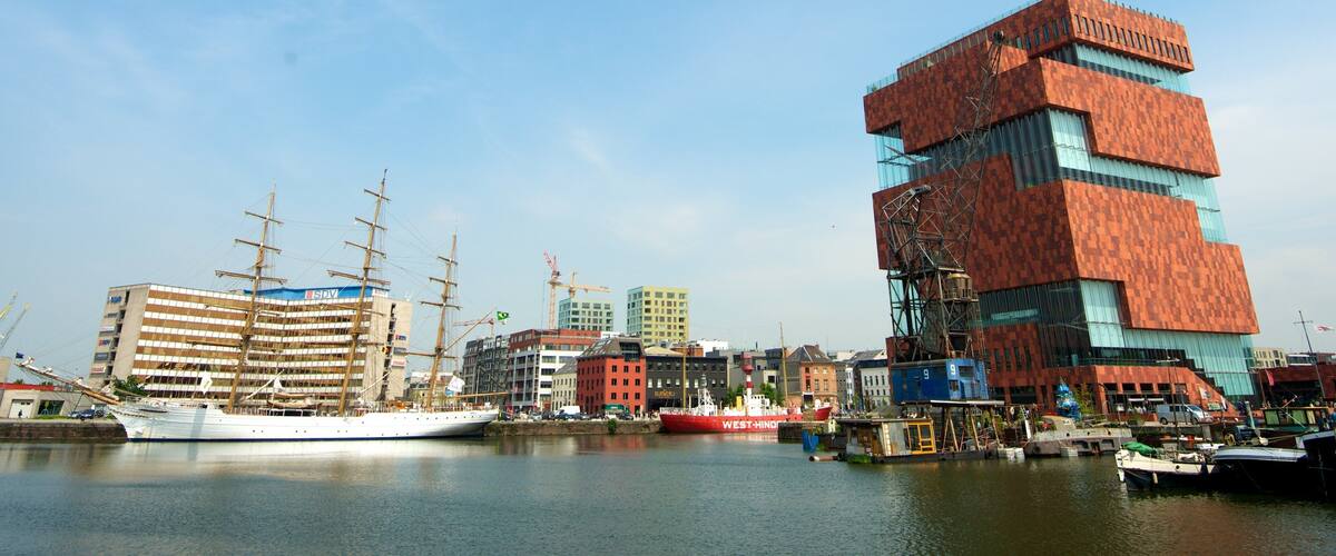 A harbor with a tall ship, modern buildings, and a distinctive red building.