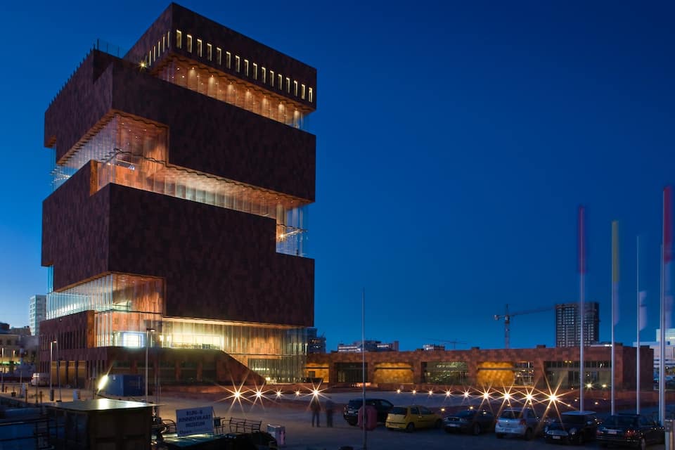 A modern building with multiple levels and illuminated windows at dusk.