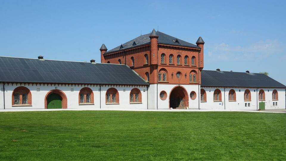 A large brick building with arched windows and a green door, surrounded by a well-maintained lawn.