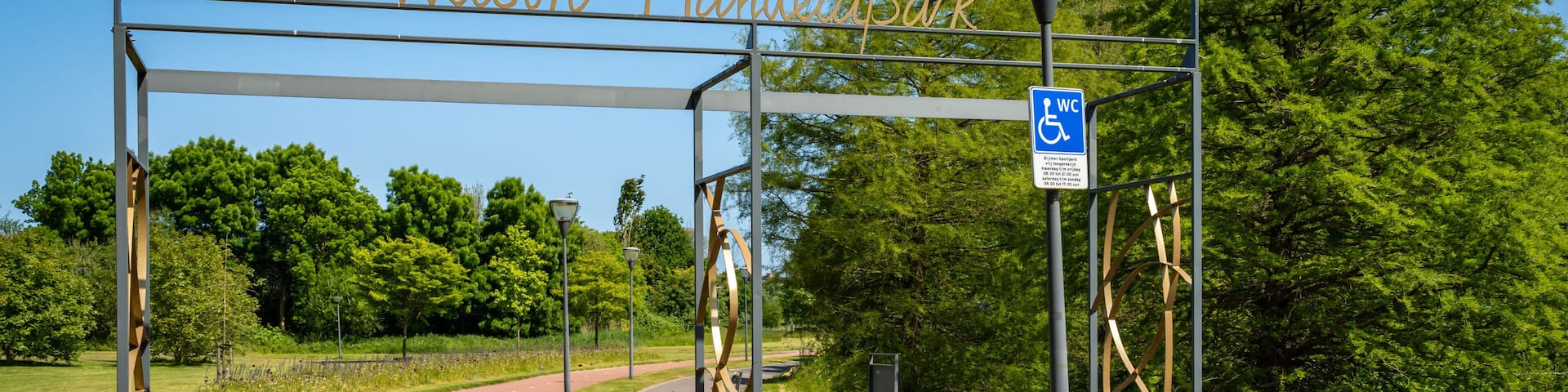 A pathway leading to Nelson Mandela Park, with a wheelchair-accessible sign and a metal gate structure.