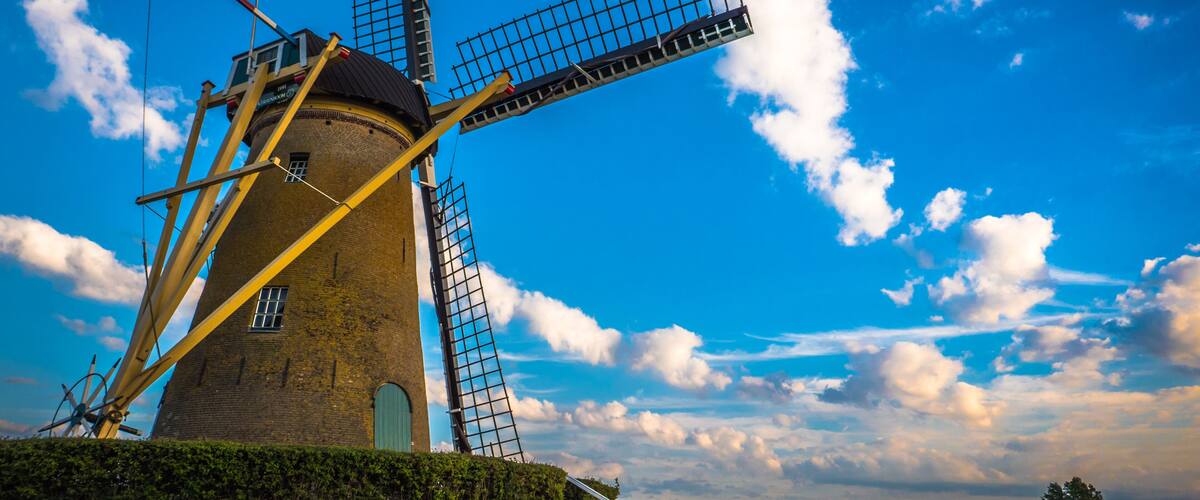 A windmill with a metal framework, set against a blue sky with clouds.