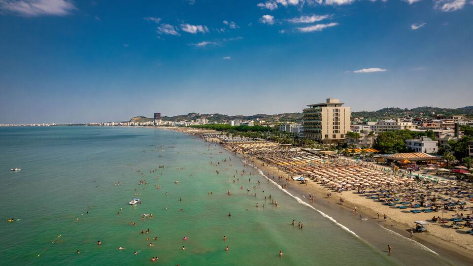 A coastal cityscape with a beach, clear blue sky, and a prominent hotel.