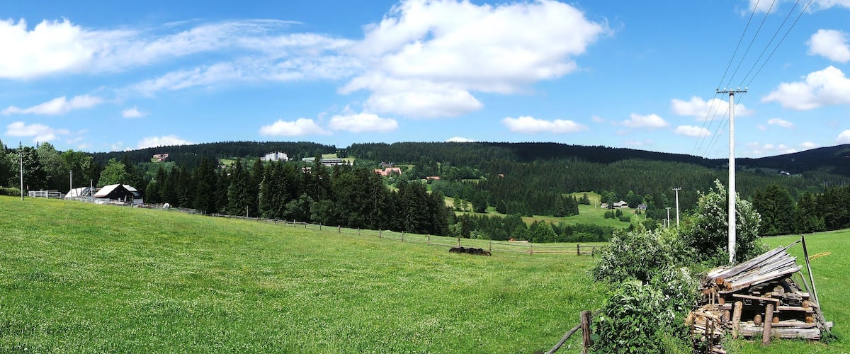 A green field with a wooden structure, a fenced area, and a distant building on a hill.