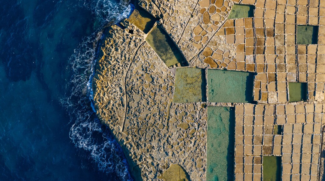 Aerial view of geometric salt pans meet the dark blue sea, creating a stunning contrast of textures and colors, Zebbug, Malta.