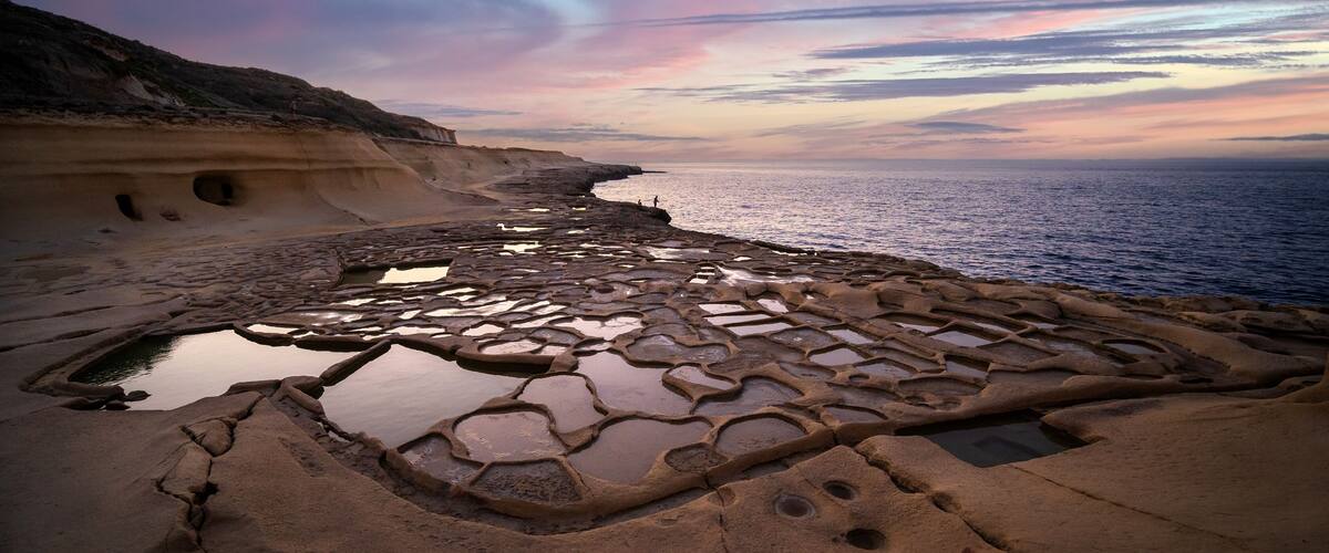 A coastal landscape with a unique rock formation featuring interconnected pools and a cliffside.