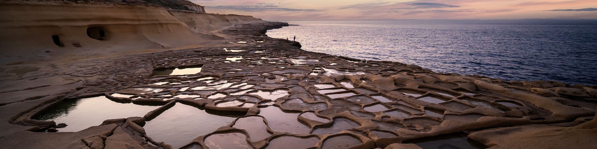 A coastal landscape with a unique rock formation featuring interconnected pools and a cliffside.