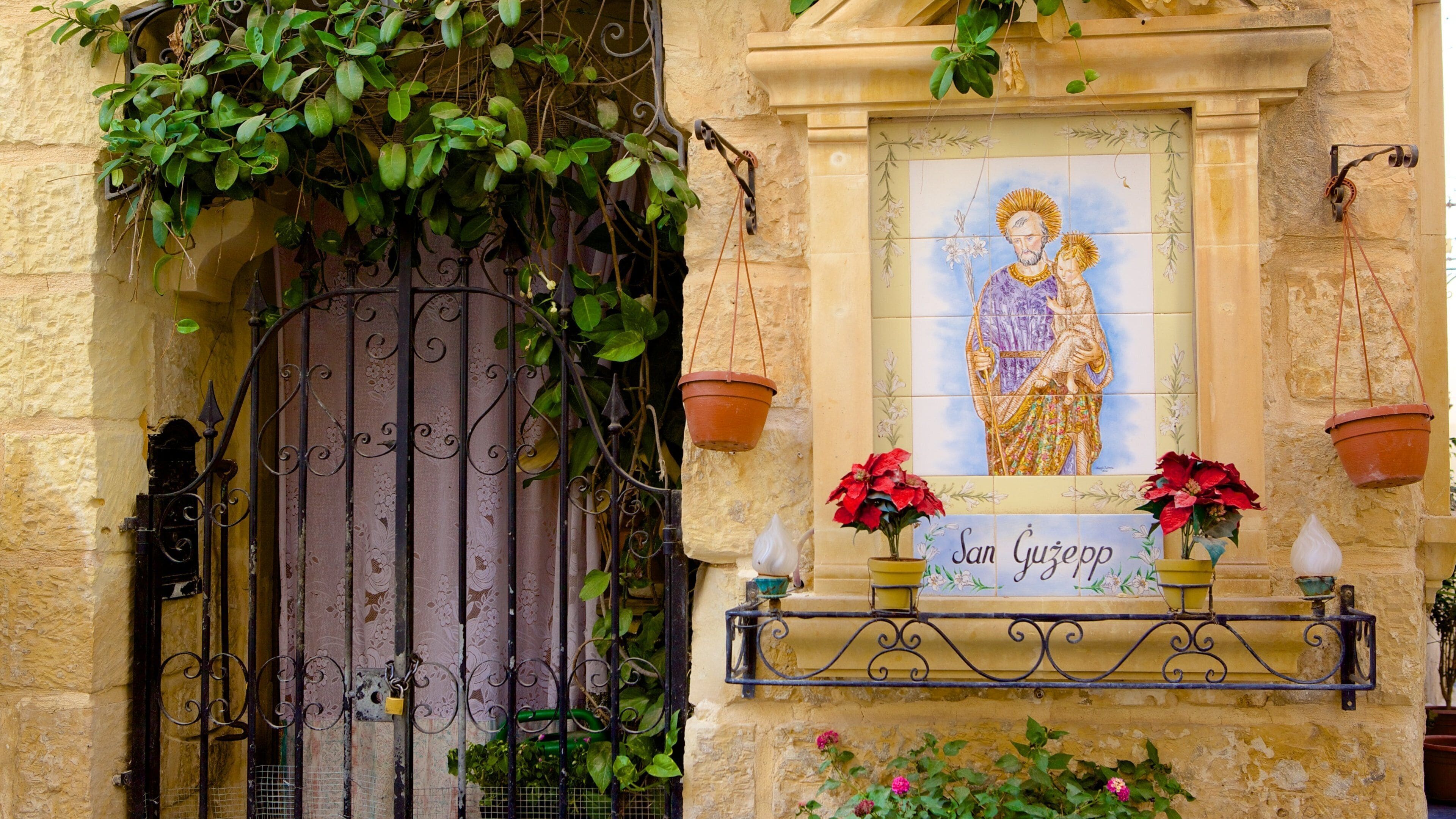 A stone building with a wrought iron gate, a mural, and potted plants.