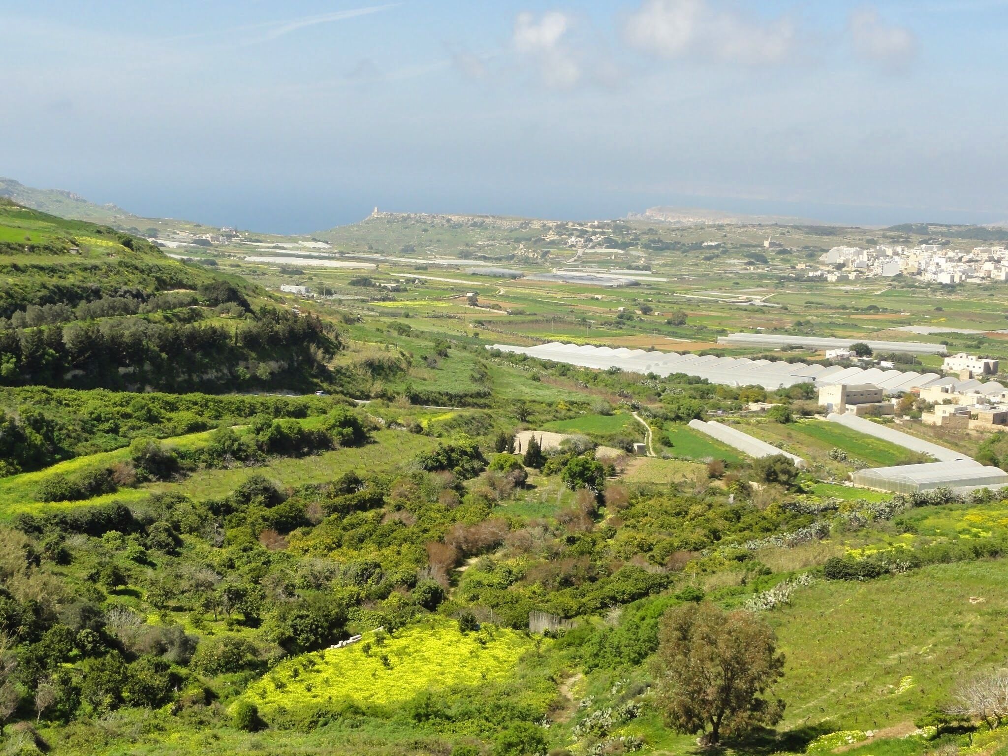 Uma paisagem verde exuberante com colinas ondulantes, uma construção fortificada ao longe e campos agrícolas.