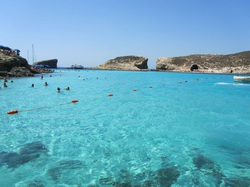 A clear turquoise sea with people swimming and a boat in the distance.