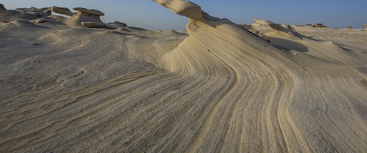 A desert landscape with prominent sand formations and layered rock structures.