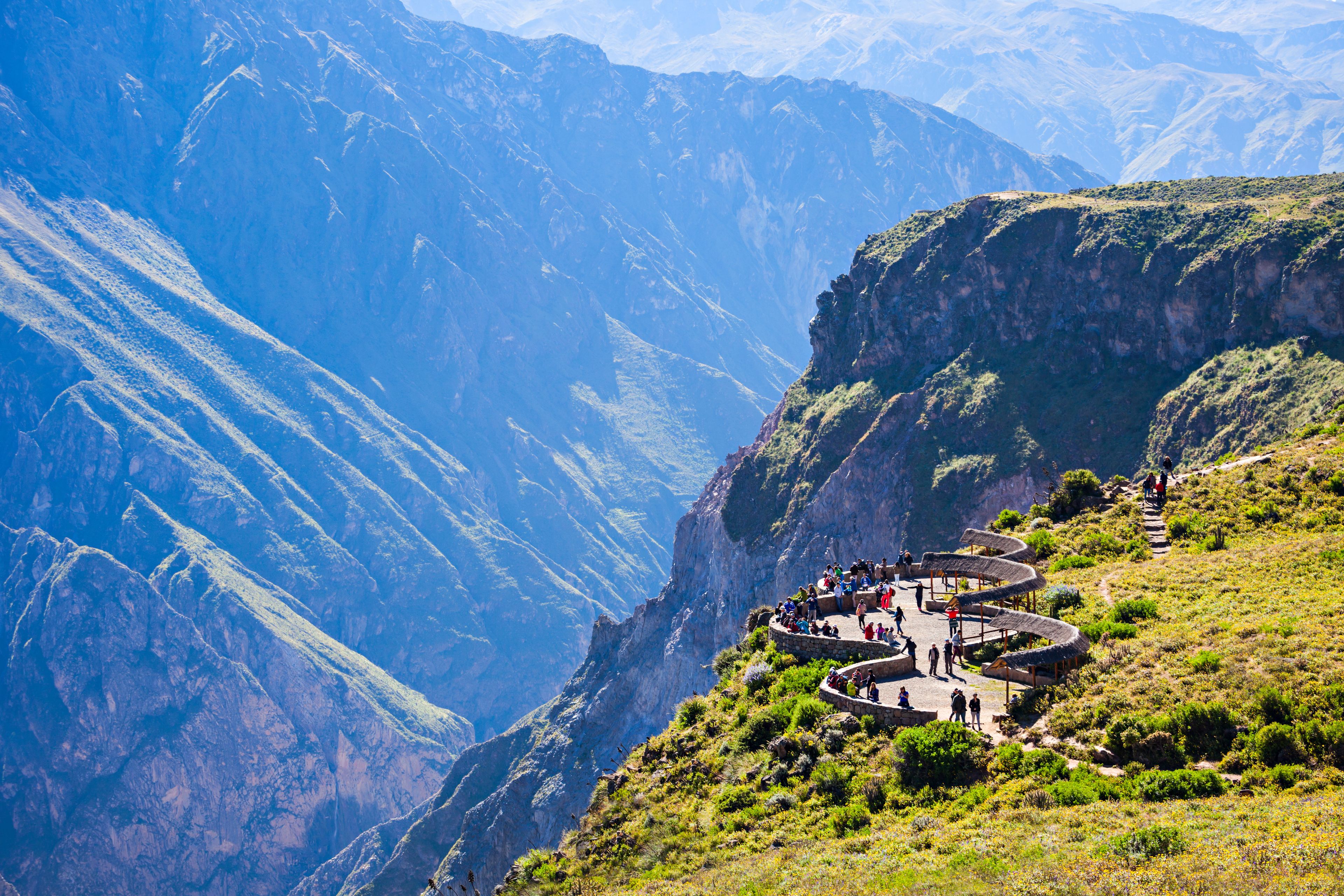 A mountainous landscape with a winding path leading to a viewing platform surrounded by lush greenery and steep cliffs.