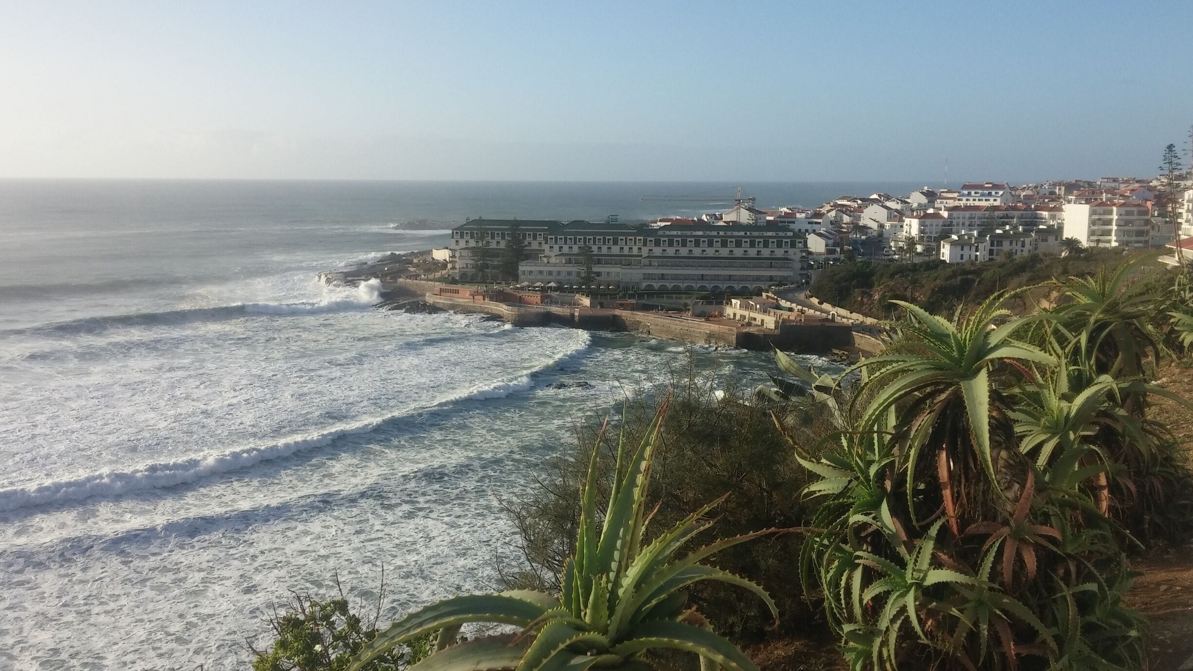 A coastal town with a rocky shoreline, waves crashing onto the beach, and buildings along the coast.