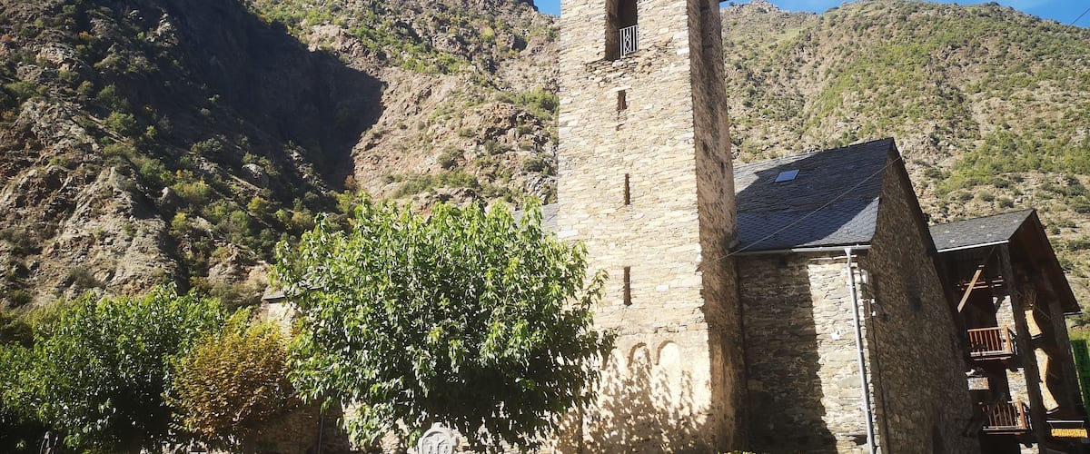 A stone church with a bell tower, surrounded by mountains and trees.