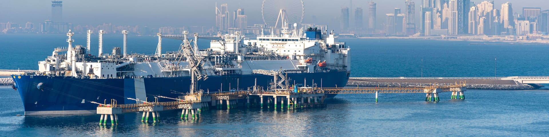 Tanker ship, LNG carrier moored in the gas terminal in the port of Jebel Ali. City skyline of Dubai visible on the horizon.