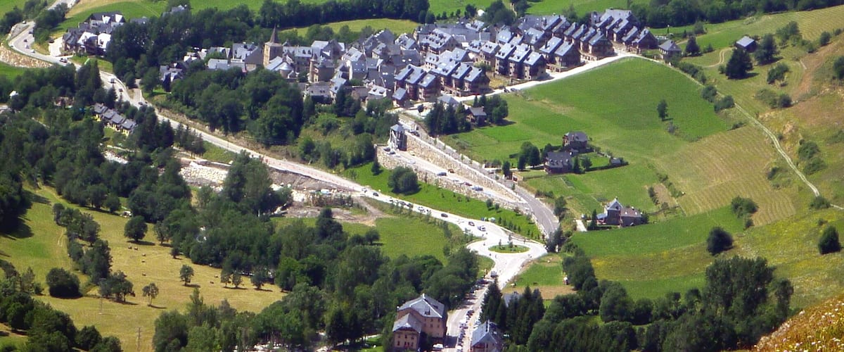 A village with a winding road, surrounded by green fields and hills.