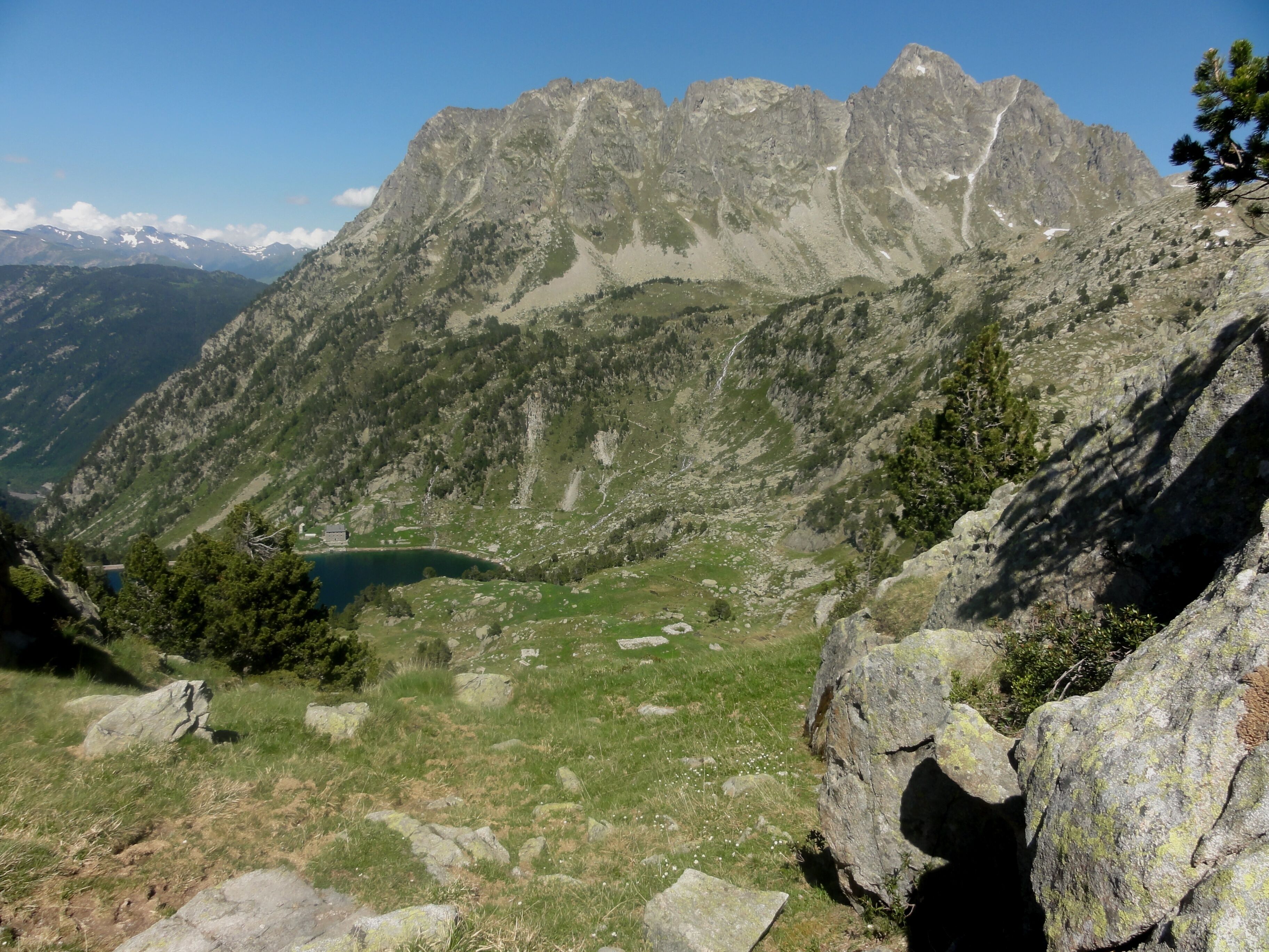 A mountainous landscape with rocky peaks, a small lake, and scattered trees.