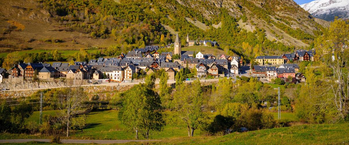 A mountain with a church, a village with traditional houses, and a snow-capped peak in the distance.