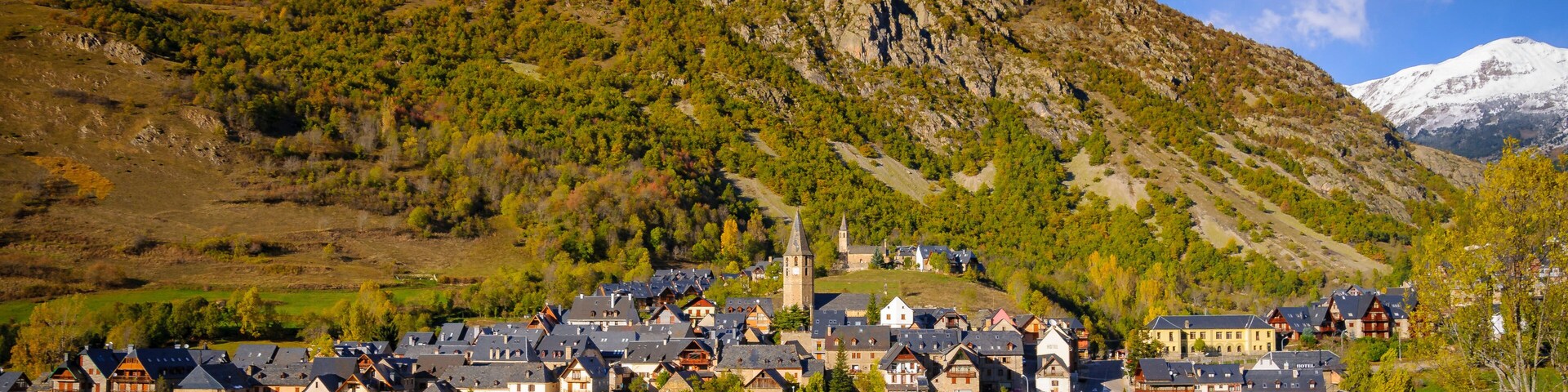 A mountain with a church, a village with traditional houses, and a snow-capped peak in the distance.