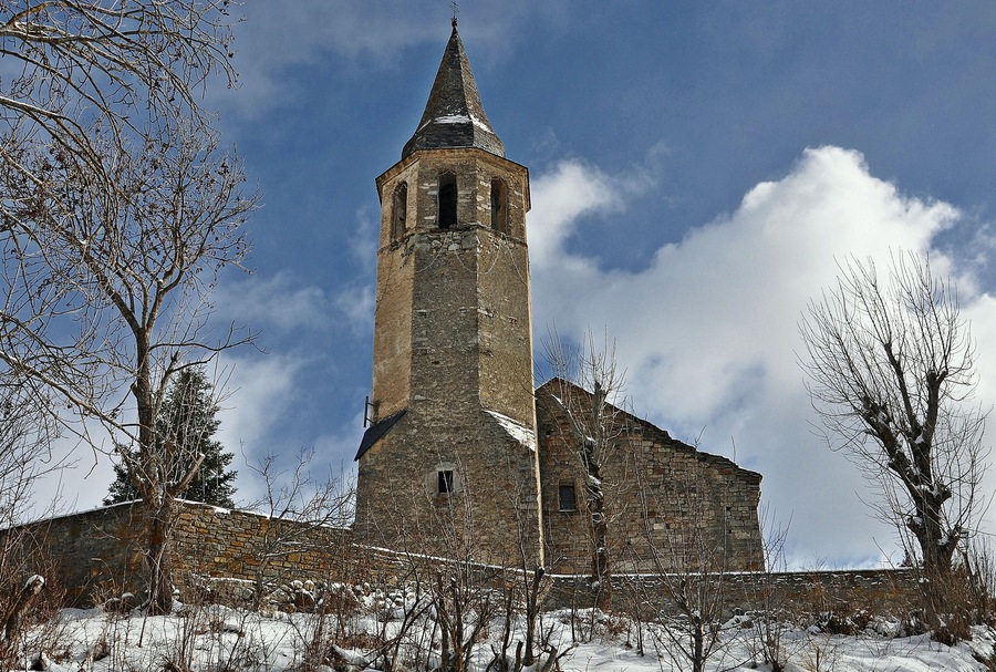 A stone church with a bell tower and a snow-covered landscape.