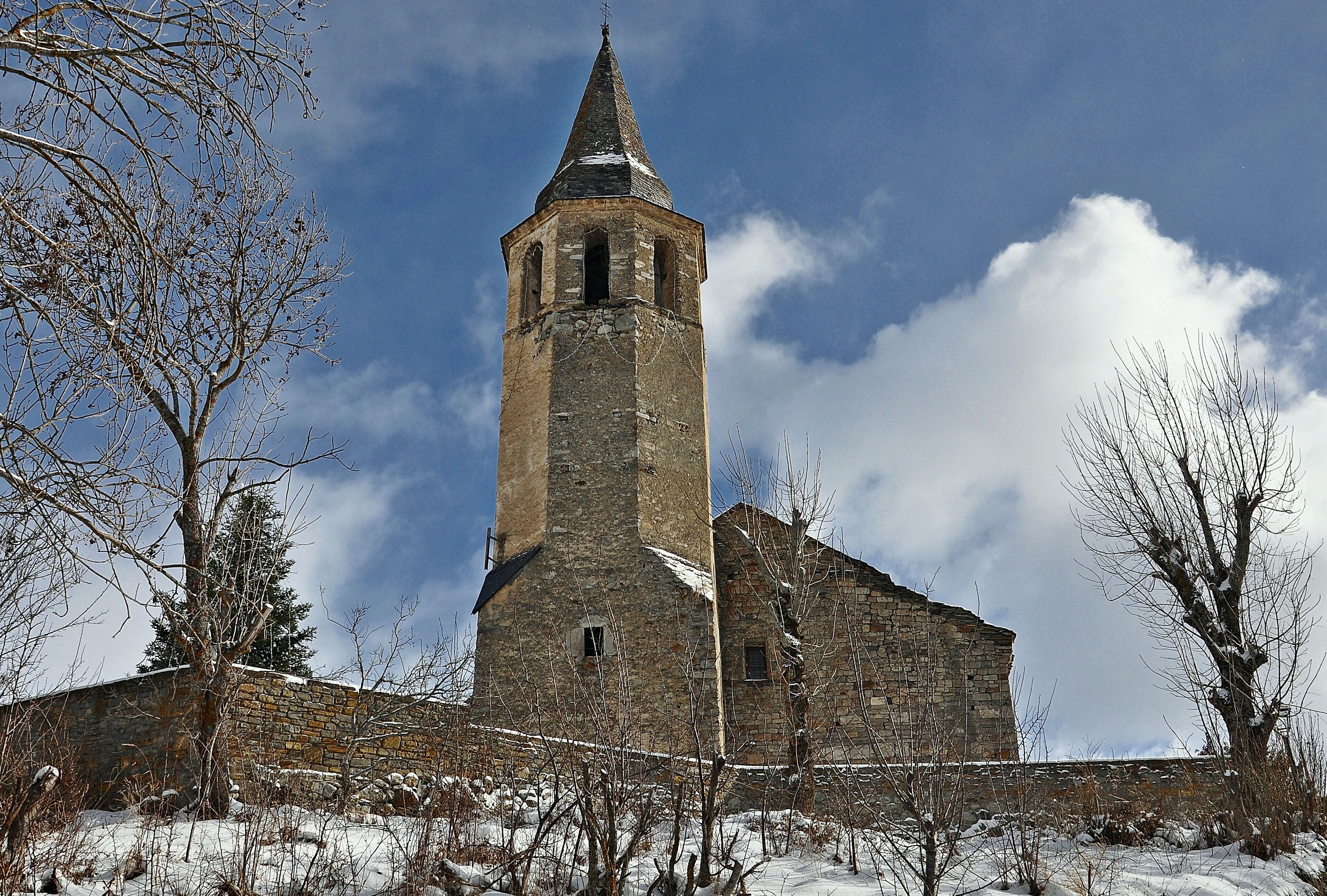 A stone church with a bell tower and a snow-covered landscape.