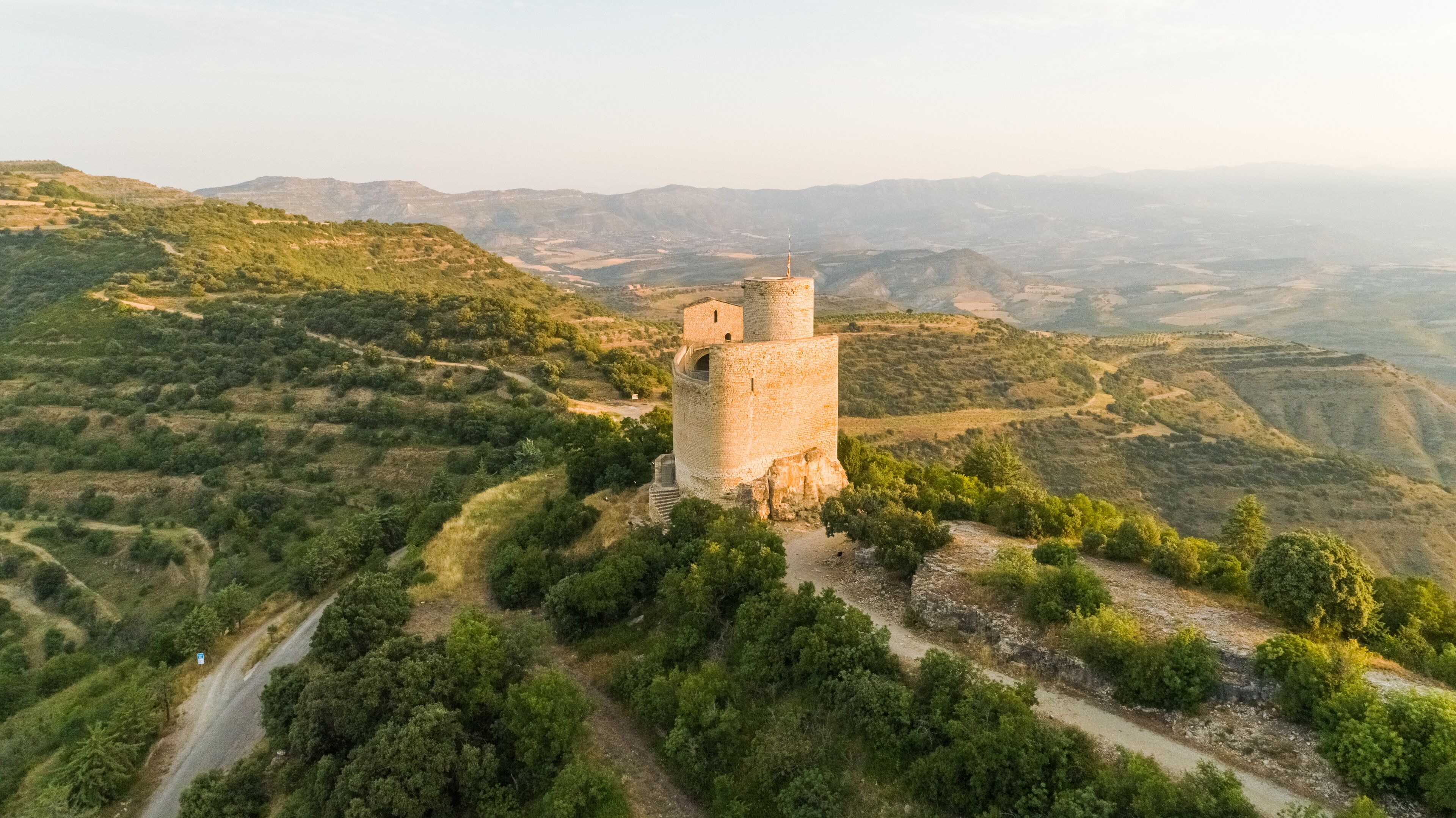 A medieval stone tower surrounded by lush greenery and rolling hills.