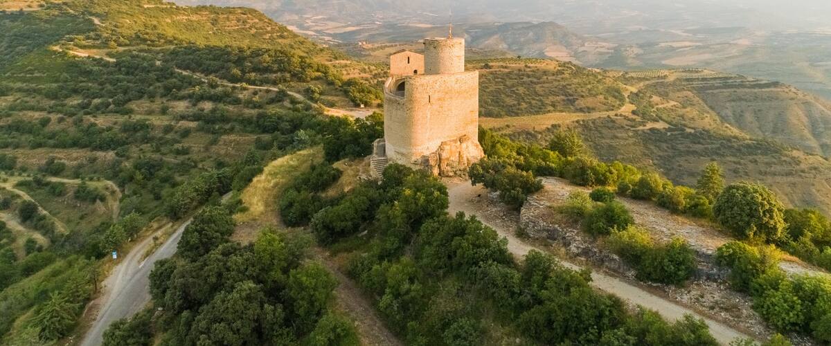 A medieval stone tower surrounded by lush greenery and rolling hills.
